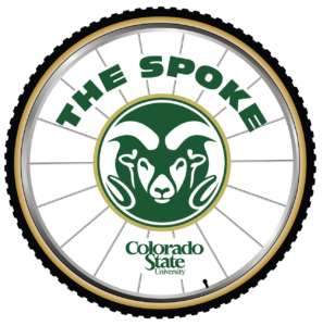 The Spoke Logo with Green Lettering, CSU Rams Head Green with Gold Accent, and Colorado State University Word Mark on a Bicycle Wheel with Black Tire and Valve Stem